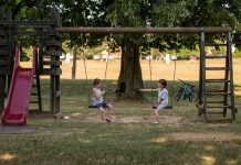 Two children playing on swings in a sunny park, capturing summer fun and friendship.