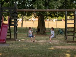 Two children playing on swings in a sunny park, capturing summer fun and friendship.