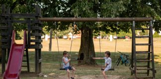 Two children playing on swings in a sunny park, capturing summer fun and friendship.