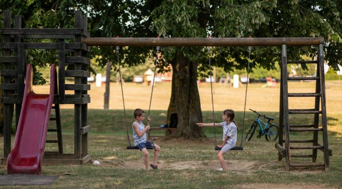 Two children playing on swings in a sunny park, capturing summer fun and friendship.