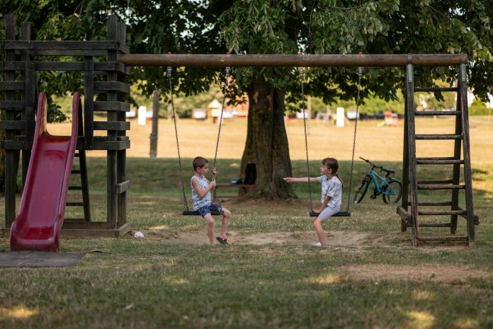 Two children playing on swings in a sunny park, capturing summer fun and friendship.
