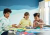 Children focusing on an art project with colored papers in a playful art class setting.