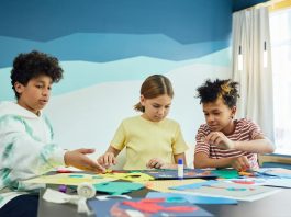 Children focusing on an art project with colored papers in a playful art class setting.