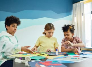 Children focusing on an art project with colored papers in a playful art class setting.