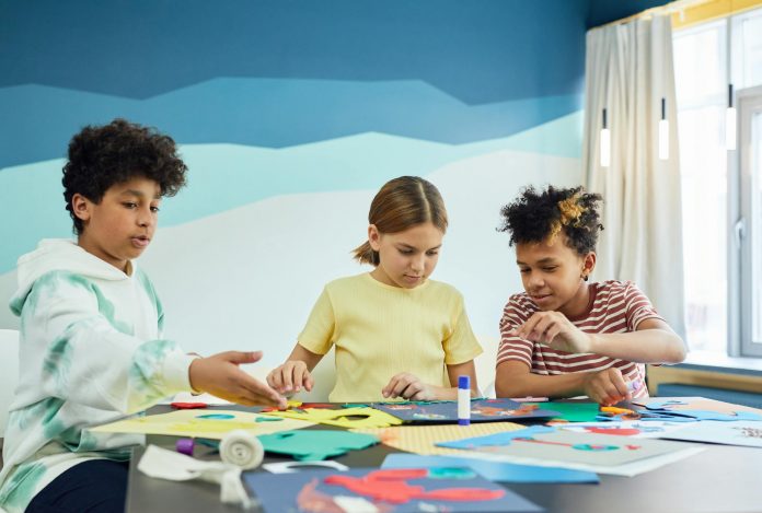 Children focusing on an art project with colored papers in a playful art class setting.