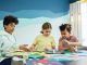 Children focusing on an art project with colored papers in a playful art class setting.