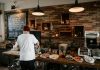 Person serving food in a cozy cafe with rustic brick walls and wooden buffet table.