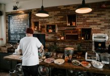 Person serving food in a cozy cafe with rustic brick walls and wooden buffet table.