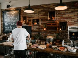 Best Breakfast in Hoboken: Your Ultimate 2026 Guide to Morning Eats Person serving food in a cozy cafe with rustic brick walls and wooden buffet table.