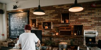 Person serving food in a cozy cafe with rustic brick walls and wooden buffet table.