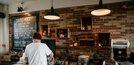 Person serving food in a cozy cafe with rustic brick walls and wooden buffet table.