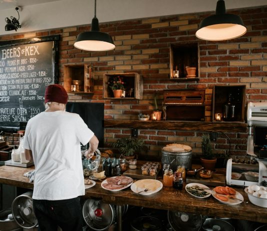 Person serving food in a cozy cafe with rustic brick walls and wooden buffet table.