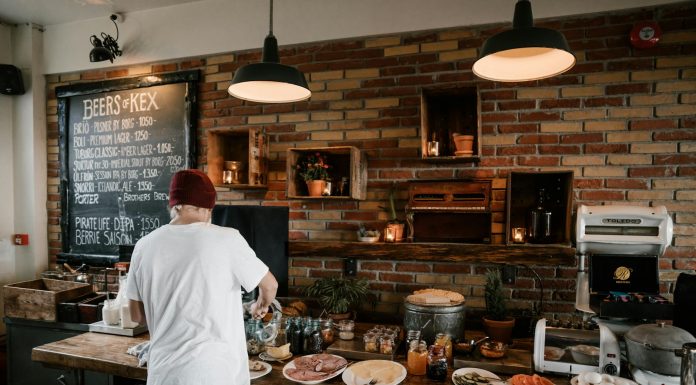 Person serving food in a cozy cafe with rustic brick walls and wooden buffet table.
