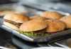 Appetizing close-up of freshly made burgers on a stainless steel tray, ready to serve.