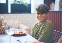 Cute child smiling at a family dining table, enjoying a meal indoors.