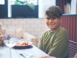 Cute child smiling at a family dining table, enjoying a meal indoors.