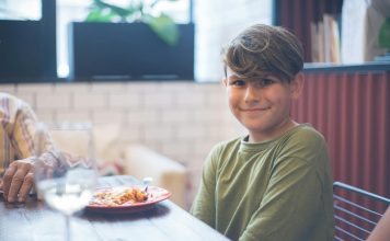 Cute child smiling at a family dining table, enjoying a meal indoors.