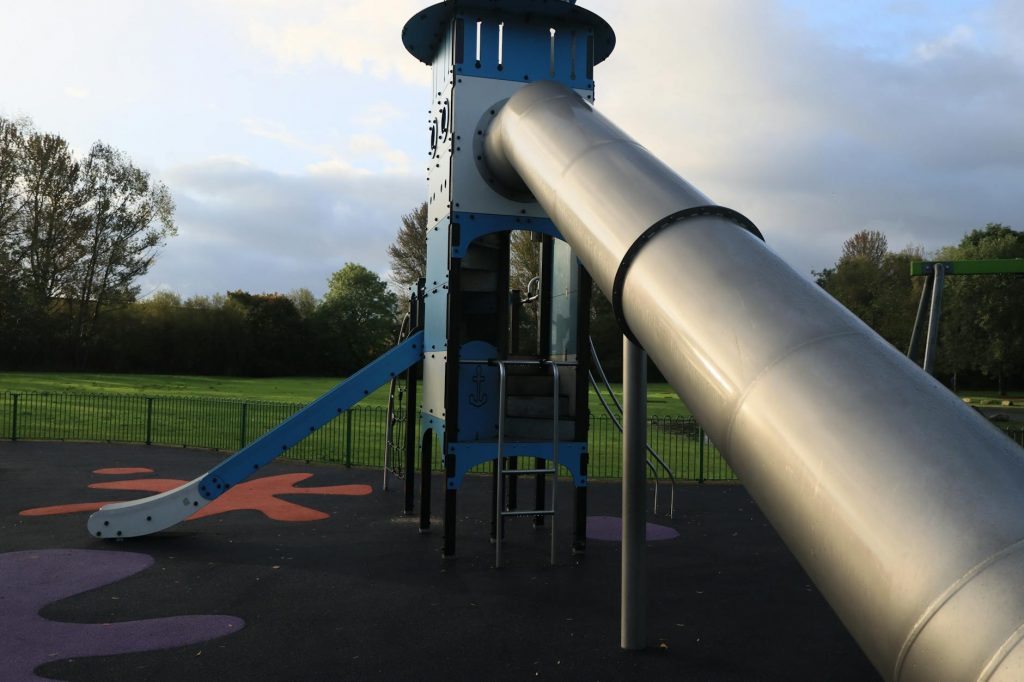A modern outdoor playground slide set in a green park in England.