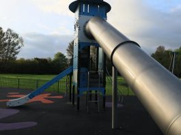 A modern outdoor playground slide set in a green park in England.