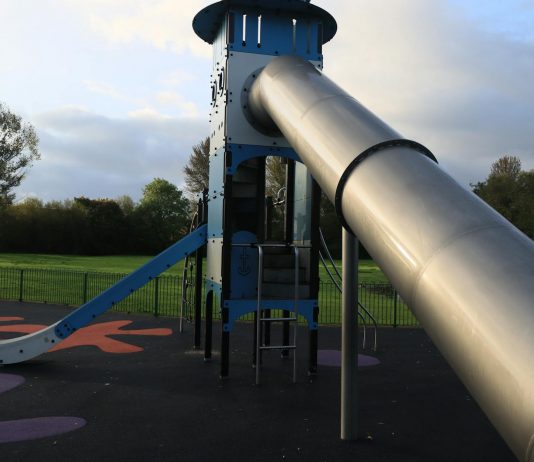 A modern outdoor playground slide set in a green park in England.