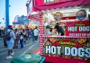 Bustling outdoor fair with a popular hot dog stand and diverse crowd.