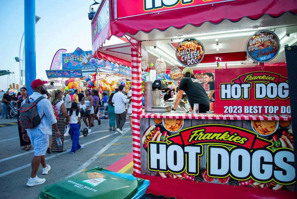 Bustling outdoor fair with a popular hot dog stand and diverse crowd.