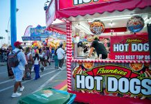Bustling outdoor fair with a popular hot dog stand and diverse crowd.