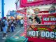 Bustling outdoor fair with a popular hot dog stand and diverse crowd.