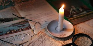 Cozy vintage scene with candle, map, glasses, and magnifying glass.