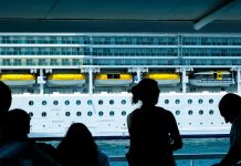 Silhouettes of people observing a large cruise ship from a dock in Türkiye.