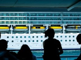 Silhouettes of people observing a large cruise ship from a dock in Türkiye.