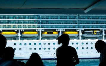 Silhouettes of people observing a large cruise ship from a dock in Türkiye.
