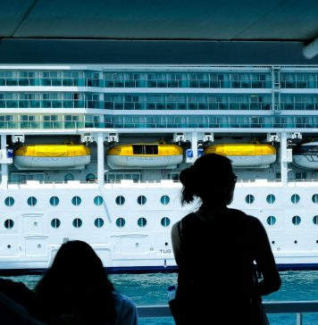 Silhouettes of people observing a large cruise ship from a dock in Türkiye.