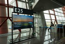 CDC seeks airport volunteers for Ebola screenings as DRC outbreak grows A view of a modern airport terminal showcasing Gate E25 with a flight display board.