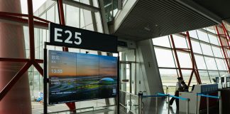 CDC seeks airport volunteers for Ebola screenings as DRC outbreak grows A view of a modern airport terminal showcasing Gate E25 with a flight display board.