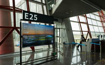 CDC seeks airport volunteers for Ebola screenings as DRC outbreak grows A view of a modern airport terminal showcasing Gate E25 with a flight display board.