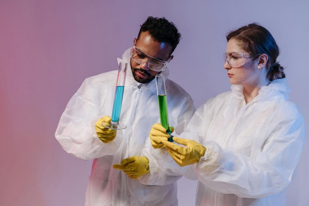 Two scientists in protective gear analyze chemical samples in a laboratory setting.