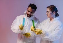 Two scientists in protective gear analyze chemical samples in a laboratory setting.