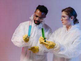 Two scientists in protective gear analyze chemical samples in a laboratory setting.