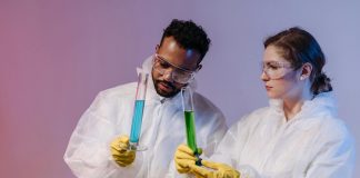 Two scientists in protective gear analyze chemical samples in a laboratory setting.