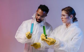 Two scientists in protective gear analyze chemical samples in a laboratory setting.