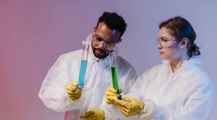 Two scientists in protective gear analyze chemical samples in a laboratory setting.
