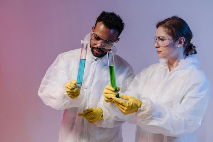 Two scientists in protective gear analyze chemical samples in a laboratory setting.