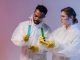 Two scientists in protective gear analyze chemical samples in a laboratory setting.