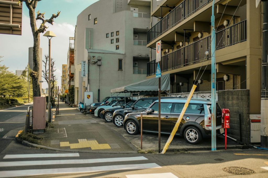 A street view capturing parked cars alongside residential buildings on a sunlit day.