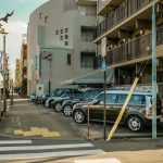 A street view capturing parked cars alongside residential buildings on a sunlit day.