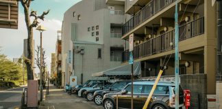 A street view capturing parked cars alongside residential buildings on a sunlit day.