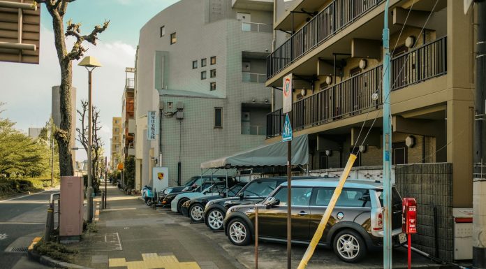 A street view capturing parked cars alongside residential buildings on a sunlit day.