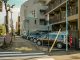 A street view capturing parked cars alongside residential buildings on a sunlit day.
