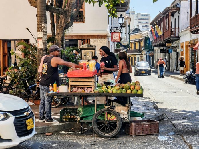 mejor-comida-colombiana-jersey-city-guia-2026 Vibrant street market scene with a fruit vendor in Cartagena, Colombia's historic district.